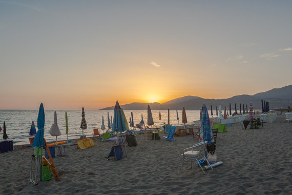 Bright umbrellas contrast with the dark sea at sunset on the coast of Italy.